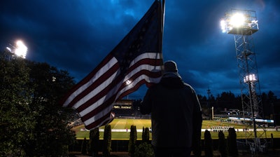 In this Wednesday, March 11, 2020 file photo, a man holds an U.S. flag as he watches the a United Soccer League match in Tacoma, Wash. In a matter of days, millions of Americans have seen their lives upended by measures to curb the spread of the new coronavirus in mid-March.