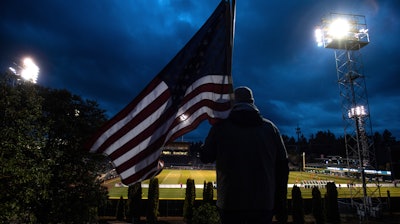 In this Wednesday, March 11, 2020 file photo, a man holds an U.S. flag as he watches the a United Soccer League match in Tacoma, Wash. In a matter of days, millions of Americans have seen their lives upended by measures to curb the spread of the new coronavirus in mid-March.