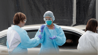 In this March 12, 2020, file photo, health care personnel test a person in the passenger seat of a car for coronavirus at a Kaiser Permanente medical center parking lot in San Francisco. The Associated Press has found that the critical shortage of testing swabs, protective masks, surgical gowns and hand sanitizer can be tied to a sudden drop in imports of medical supplies.