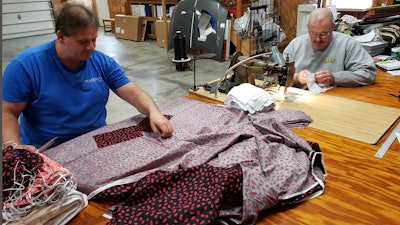 In this Sunday, March 22, 2020 photo, Bill Purdue, left, cuts pieces of fabric while Mike Rice sews them into face masks in Rice's autobody and upholstery shop in Washington, Ind.