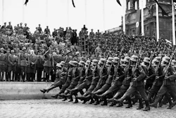 In this March 24, 1938, file photo, German standard bearers parade past Maj. Gen. Fedor von Bock, commander of all armed forces in the Austrian territory, center, on grandstand on the Kingstrasse in front of the Memorial of Honor, as the troops reach Vienna. Beside him wearing overcoat is Dr. Seysz Incuart. World War II references are now heard daily, not because another momentous 75th anniversary, Victory in Europe Day approaches in May but because of the coronavirus.