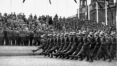 In this March 24, 1938, file photo, German standard bearers parade past Maj. Gen. Fedor von Bock, commander of all armed forces in the Austrian territory, center, on grandstand on the Kingstrasse in front of the Memorial of Honor, as the troops reach Vienna. Beside him wearing overcoat is Dr. Seysz Incuart. World War II references are now heard daily, not because another momentous 75th anniversary, Victory in Europe Day approaches in May but because of the coronavirus.