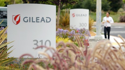 In this July 9, 2015, file photo, a man walks outside the headquarters of Gilead Sciences in Foster City, Calif. Gilead Sciences said Wednesday, March 25, 2020 it will give up the specialty status it received days earlier for its COVID-19 drug amid public outrage that the company was seeking to boost the profits of its treatment.