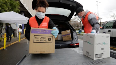 Volunteers Keshia Link, left, and Dan Peterson unload boxes of donated gloves and alcohol wipes from a car at a drive-up donation site for medical supplies at the University of Washington to help fight the coronavirus outbreak Tuesday, March 24, 2020, in Seattle.