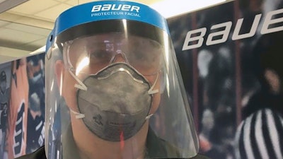 In this March 23, 2020, photo provided by Bauer Hockey Corp., an employee models a medical face shield the hockey equipment manufacturer has begun creating to help those treating the coronavirus pandemic, at Bauer Hockey Corp. in Blainville, Quebec.
