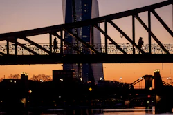 Two women walk over a bridge with the European Central Bank in background in Frankfurt, Germany, as the sun rises Monday, March 30, 2020. Due to the coronavirus the economy expects heavy losses. For most people, the new coronavirus causes only mild or moderate symptoms, such as fever and cough. For some, especially older adults and people with existing health problems, it can cause more severe illness, including pneumonia.