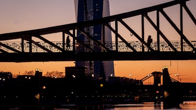 Two women walk over a bridge with the European Central Bank in background in Frankfurt, Germany, as the sun rises Monday, March 30, 2020. Due to the coronavirus the economy expects heavy losses. For most people, the new coronavirus causes only mild or moderate symptoms, such as fever and cough. For some, especially older adults and people with existing health problems, it can cause more severe illness, including pneumonia.