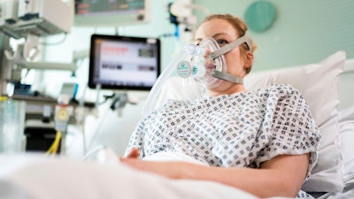 In this Friday, March 27, 2020 photo provided by UCLH a female volunteer demonstrates the use of a CPAP device at UCL Hospital in London.