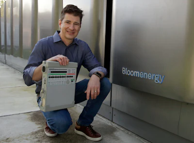 Joe Tavi, Bloom Energy senior director of manufacturing, holds a refurbished ventilator as he kneels beside fuel cells, Wednesday, April 1, 2020, in Sunnyvale, Calif. The new coronavirus outbreak has prompted companies large and small to rethink how they do business. Bloom Energy, in San Jose, Calif., makes hydrogen fuel cells. But recently, they have been refurbishing old ventilators so hospitals can use them to keep coronavirus patients alive.