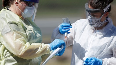 In this Tuesday, March 31, 2020 file photo, medical technicians handle a vial containing a nasal swab at a drive-thru testing site in Wheat Ridge, Colo., as a statewide stay-at-home order remains in effect in an effort to reduce the spread of the COVID-19 coronavirus.