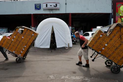 Workers pull dollies loaded with boxes of produce past a decontamination tent at the Centro de Abastos, the main food distribution center in Mexico City, Tuesday, April 7, 2020. The tent was set up a measure to help slow down the spread of the new coronavirus pandemic.