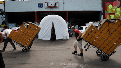 Workers pull dollies loaded with boxes of produce past a decontamination tent at the Centro de Abastos, the main food distribution center in Mexico City, Tuesday, April 7, 2020. The tent was set up a measure to help slow down the spread of the new coronavirus pandemic.