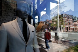 A passer-by wearing a mask out of concern for the COVID-19 coronavirus, background center, walks past mannequins in a clothing store in Boston.
