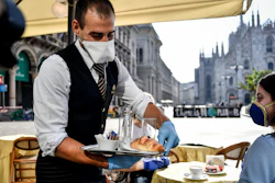 Two girls have breakfast served at a bar in front of the gothic Cathedral in Milan, May 18, 2020.