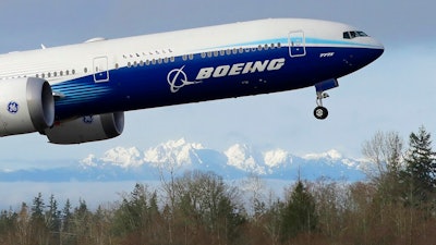 In this Jan. 25, 2020, file photo a Boeing 777X airplane takes off on its first flight with the Olympic Mountains in the background at Paine Field in Everett, Wash. Boeing on Wednesday, May 27, is cutting more than 12,000 jobs through layoffs and buyouts as the coronavirus pandemic seizes the travel industry. And the aircraft maker says more cuts are coming.