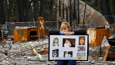 In this Feb. 7, 2019, file photo, Christina Taft, the daughter of Camp Fire victim Victoria Taft, displays a collage of photos of her mother, at the burned out ruins of the Paradise, Calif., home where she died in 2018. Pacific Gas & Electric officials are to be expected to appear in court Tuesday, June 16, 2020, to plead guilty for the deadly wildfire that nearly wiped out the Northern California town of Paradise in 2018.