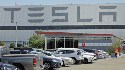 In this Monday, May 11, 2020 file photo, a man wearing a mask walks through the Tesla plant parking lot in Fremont, Calif. On Wednesday, July 22, 2020, the electric car maker announced it has picked the Austin, Texas, area as the site for its largest auto assembly plant employing at least 5,000 workers.