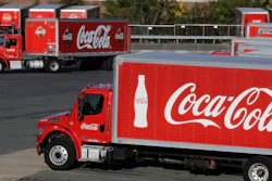 In this Oct. 14, 2019 file photo, a truck with the Coca-Cola logo, behind left, maneuvers in a parking lot at a bottling plant in Needham, MA.