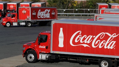 In this Oct. 14, 2019 file photo, a truck with the Coca-Cola logo, behind left, maneuvers in a parking lot at a bottling plant in Needham, MA.