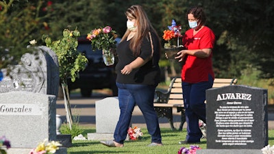 Lori Gonzalez, left, and Rachel Spray carry flowers to the temporary grave marker of Gonzalez's sister and Kaiser Permanente Fresno Medical Center nurse, Sandra Oldfield, at the Sanger Cemetery in Sanger, Calif., Saturday, Aug. 29, 2020.