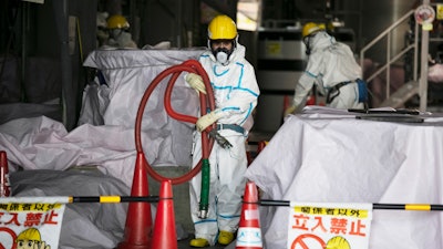 A worker in a hazmat suit carries a hose at the Fukushima Dai-ichi nuclear power plant, Okuma, Japan, Feb. 12, 2020.