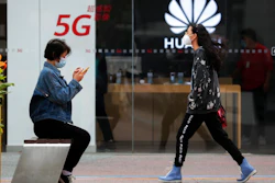 A woman wearing a face mask to help curb the spread of the coronavirus browses her smartphone as a masked woman walks by the Huawei retail shop promoting it 5G network in Beijing on Oct. 11, 2020. Chinese leaders are meeting to formulate an economic blueprint for the next five years that is expected to emphasize development of semiconductors and other technology amid a feud with Washington that is cutting off access to U.S. components for China's fledgling tech industries.
