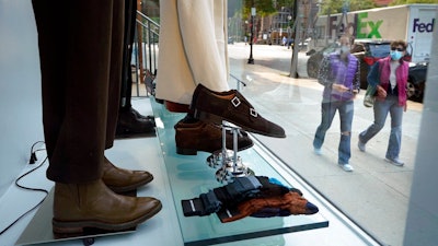 In this Tuesday, Sept. 15, 2020, file photo, passers-by examine a storefront window in Boston's fashionable Newbury Street shopping district. U.S. consumer confidence dipped slightly in October as a new wave of coronavirus cases began across the country. The Conference Board reported Tuesday, Oct. 27, 2020, that its consumer confidence index fell to a reading of 100.9, from 101.8 in September.