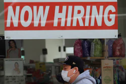 A man wearing a mask while walking under a Now Hiring sign at a CVS Pharmacy.