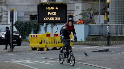 A woman cycles on a Brompton folding bicycle past a sign outside Waterloo Station reminding people they are required to wear face coverings inside the station and whilst traveling on trains, in London, during England's second coronavirus lockdown, Friday, Nov. 20, 2020.