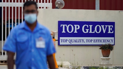 A worker from Top Glove walks outside Top Glove factory in Shah Alam, Malaysia, Wednesday, Nov. 25, 2020. Malaysia's Top Glove Corp., the world's largest maker of rubber gloves, says it expects a two to four-week delay in deliveries after more than 2,000 workers at its factories were infected by the coronavirus, raising the possibility of supply disruptions during the pandemic.