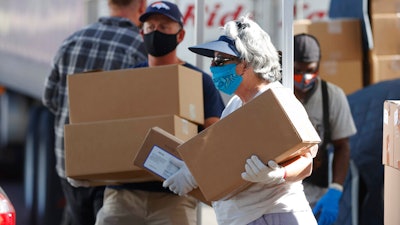 Volunteers Juanita MacKenzie, front, and Dave Stutman carry boxes of food to a waiting car at a pantry.