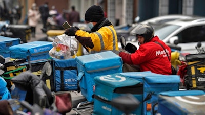 A food delivery worker wearing a face mask to help curb the spread of the coronavirus prepares to deliver foods for his customers outside a restaurant in Beijing on Thursday, Jan. 14, 2021. The e-commerce workers and delivery people who kept China fed during the pandemic, making their billionaire bosses even richer, are so unhappy with their pay and treatment that one just set himself on fire in protest.