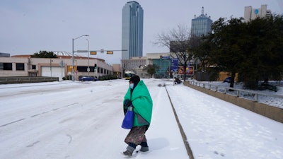 In this Feb. 16, 2021, file photo, a woman wrapped in a blanket crosses the street near downtown Dallas. As temperatures plunged and snow and ice whipped the state, much of Texas' power grid collapsed, followed by its water systems. Tens of millions huddled in frigid homes that slowly grew colder or fled for safety.