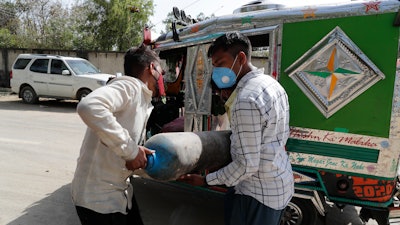 People carry a medical oxygen cylinder at a charging station on the outskirts of Prayagraj, India, Friday, April 23, 2021. India put oxygen tankers on special express trains as major hospitals in New Delhi on Friday begged on social media for more supplies to save COVID-19 patients who are struggling to breathe. India's underfunded health system is tattering as the world's worst coronavirus surge wears out the nation, which set another global record in daily infections for a second straight day with 332,730.