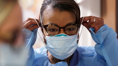 In this Friday, May 8, 2020 file photo, a respiratory therapist pulls on a second mask over her N95 mask before adding a face shield as she gets ready to go into a patient's room in the COVID-19 Intensive Care Unit at a hospital in Seattle. Medical providers may soon return to using one medical N95 mask per patient, a practice that was suspended during the pandemic due to deadly supply shortages.