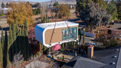 This photo provided by Mighty Buildings shows a 3D-printed housing module being delivered. Most of the modules built by Mighty Buildings are assembled in the factory, transported by truck to the owner’s property, then put into place using a crane.