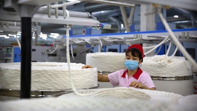 A worker watches as a machine processes cotton yarn at a Huafu Fashion plant, Aksu, China, April 20, 2021.