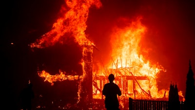 In this Nov. 8, 2018 file photo, a home burns as a wildfire called the Camp Fire rages through Paradise, Calif. A trust approved by a federal judge to help compensate victims of deadly California wildires sparked by Pacific Gas & Electric equipment paid survivors just $7 million while racking up $51 million in overhead in its first year of operation, KQED News reported.