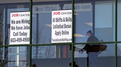 In this file photo, a woman, wearing a protective mask due to the COVID-19 virus outbreak, walks past the signs of an employment agency, in Manchester, NH.