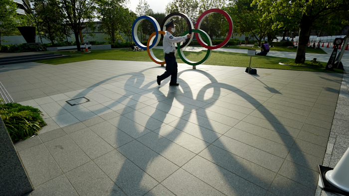 In this May 9, 2021, file photo, a security guard wearing a protective mask to help curb the spread of the coronavirus walks in front of the Olympic Rings, in Tokyo. Japan, seriously behind in coronavirus vaccination efforts, is scrambling to boost daily shots as the start of the Olympics in July closes in.