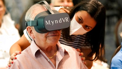 Gloria Gantes, right, monitors Terry Colli, a resident of John Knox Village, as he participates in a virtual reality study, June 1, 2021, Pompano Beach, Fla.