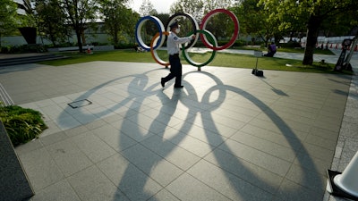 In this May 9, 2021, file photo, a security guard wearing a protective mask to help curb the spread of the coronavirus walks in front of the Olympic Rings, in Tokyo. Japan, seriously behind in coronavirus vaccination efforts, is scrambling to boost daily shots as the start of the Olympics in July closes in.