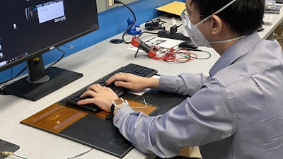 Sunghoon Ivan Lee demonstrates how the wearable device is charged through his left forearm's contact with the power transmitter below the keyboard.