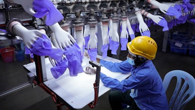 In this Aug. 26, 2020, file photo, a worker inspects disposable gloves at the Top Glove factory in Shah Alam outside Kuala Lumpur, Malaysia. Malaysia's Top Glove Corp., the world's largest rubber glove maker, said in May, 2021, it hopes to swiftly end a U.S. ban on its products due to allegations of forced labor after one of its shipment was seized at a U.S. port. Malaysia's government pledged Monday, July 5, 2021, to take steps to eliminate forced labor after the country was downgraded by the U.S. to the worst level in an annual report on human trafficking.