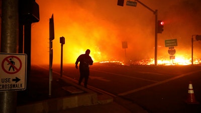 In this Oct. 11, 2019, file photo, a bystander watches the Saddleridge Fire in Sylmar, Calif. Pacific Gas & Electric plans to bury 10,000 miles of its power lines in an effort to prevent its fraying grid from sparking wildfires when electrical equipment collides with millions of trees and other vegetation sprawling across its drought-stricken service.