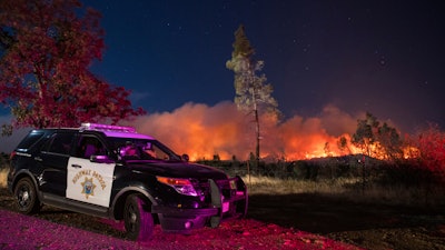 In this Sept. 28. 2020, file photo, a California Highway Patrol officer watches flames visible from the Zogg Fire near Igo, Calif. Pacific Gas & Electric is facing criminal charges because its equipment sparked the wildfire that killed four people and destroyed hundreds of homes, a Northern California prosecutor announced Thursday, July 29, 2021.