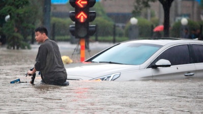 A man rides a bicycle through a flooded intersection in Zhengzhou in central China's Henan Province, Tuesday, July 20, 2021. China's military has blasted a dam to release floodwaters threatening one of its most heavily populated provinces.