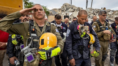 A member of the Israeli search and rescue team, left, salutes in front of the rubble that once was Champlain Towers South during a prayer ceremony, Wednesday, July 7, 2021, in Surfside, Fla.