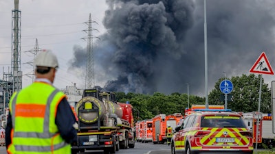 Emergency vehicles of the fire brigade, rescue services and police stand not far from an access road to the Chempark over which a dark cloud of smoke is rising in Leverkusen, Germany, Tuesday, July 27, 2021.