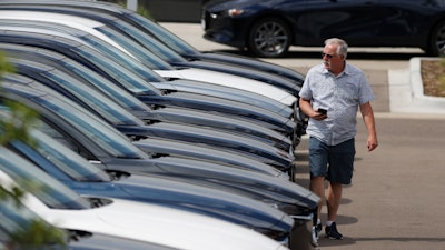 In this Sunday, June 14, 2020, photograph, a prospective buyer looks over a long row of unsold 2020 CX-5 sports-utility vehicles sedans sits at a Mazda dealership in Littleton, Colo.